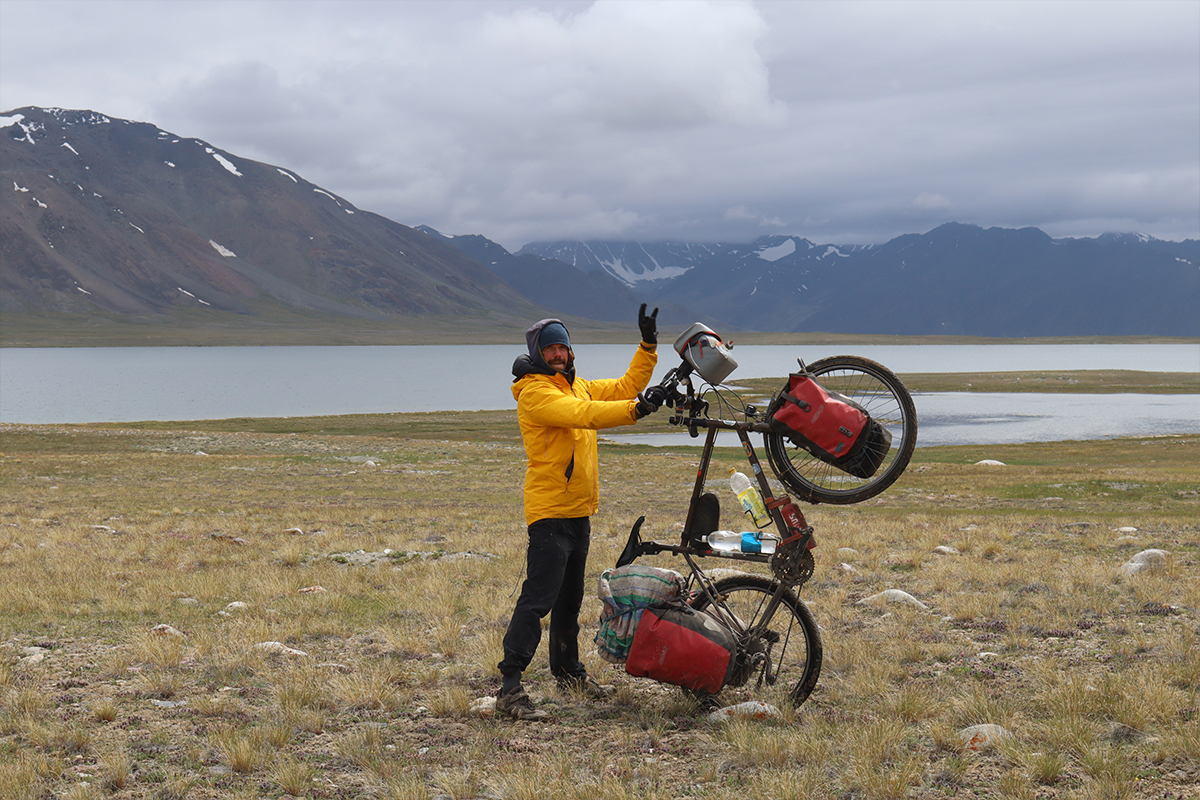 Guy holding a bike on an mountain landscape.